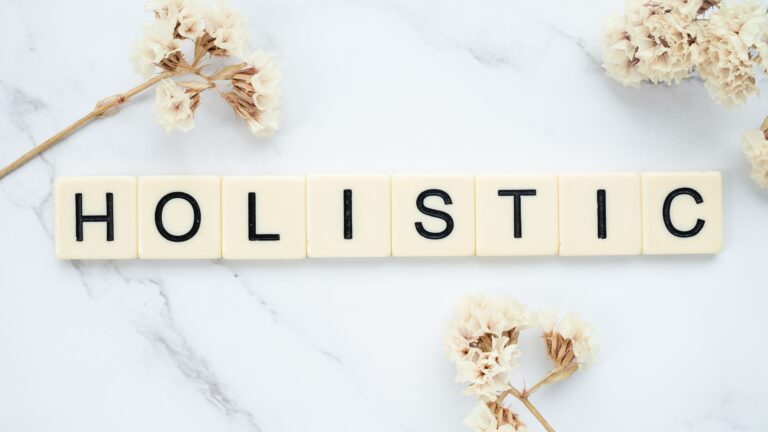 Somos holísticos Flat lay of 'holistic' spelled in letter tiles on marble with dried flowers.